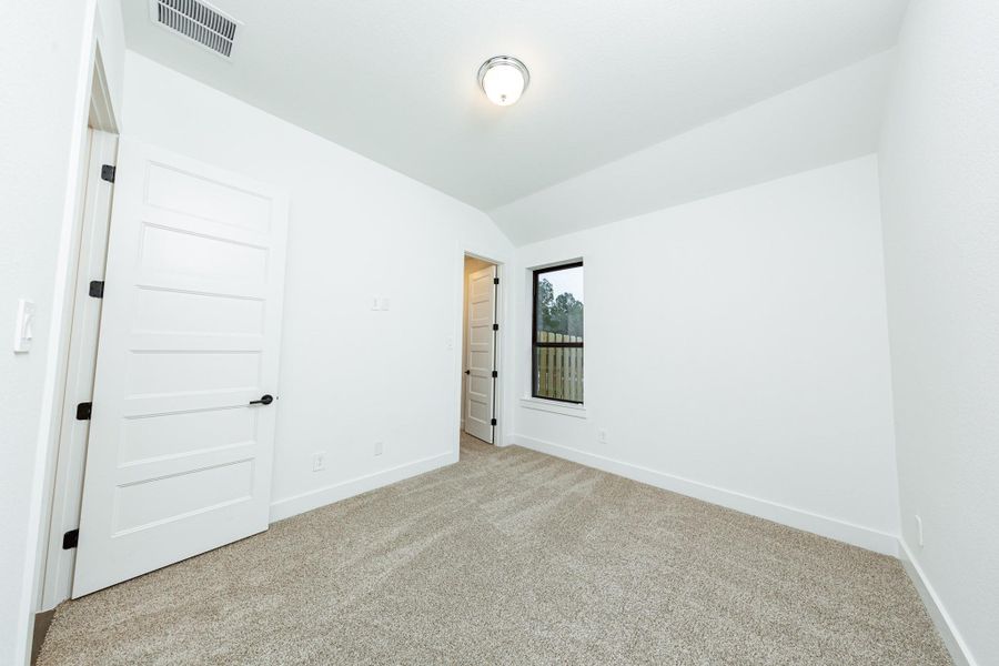 This secondary bedroom features a sloped ceiling, plush carpet flooring, a large window, a walk-in closet, and an ensuite secondary bathroom.