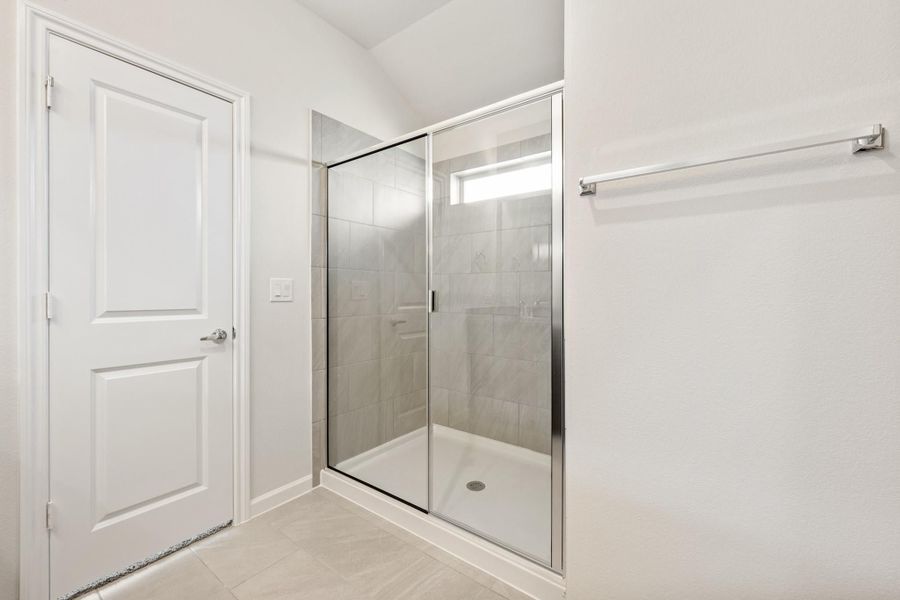Walk-in shower with glass sliding door, gray tile walls, and chrome fixtures in a white bathroom