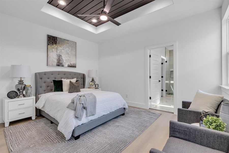 Bedroom with ceiling fan, ensuite bath, light wood-type flooring, and a tray ceiling