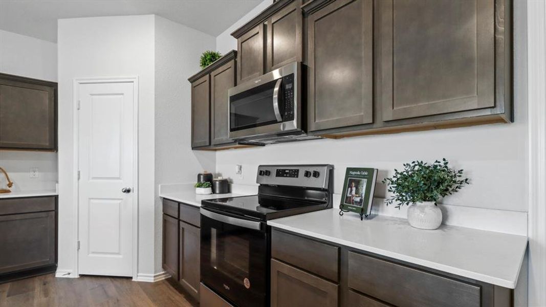 Kitchen featuring dark wood-finish cabinetry, light countertops, stainless steel appliances, and wood-finish flooring