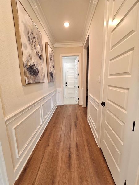 This hallway features elegant wood flooring, decorative wall paneling, and modern art pieces. It leads to a room with white paneled doors, providing a clean and sophisticated look.