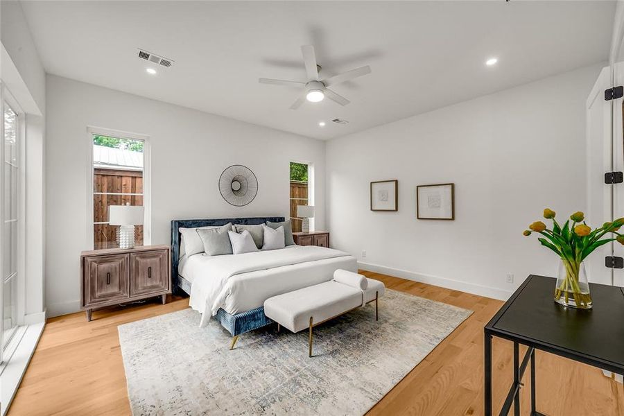 Spacious bedroom featuring light wood-finish flooring, white walls, recessed lighting, a ceiling fan, and multiple windows