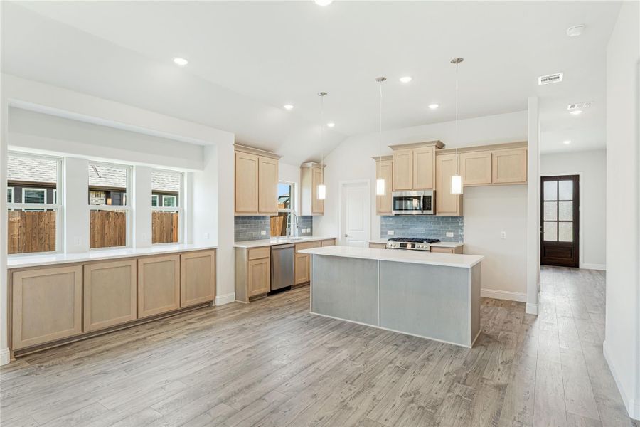 Open kitchen with light wood cabinets, center island, gray tile backsplash, and hardwood floors Open kitchen with light wood cabinets, center island, gray tile backsplash, and hardwood floors