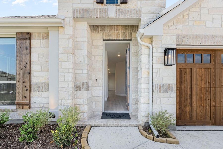 Home entrance with open front door, limestone exterior, wood shutters, and welcome mat Home entrance with open front door, limestone exterior, wood shutters, and welcome mat