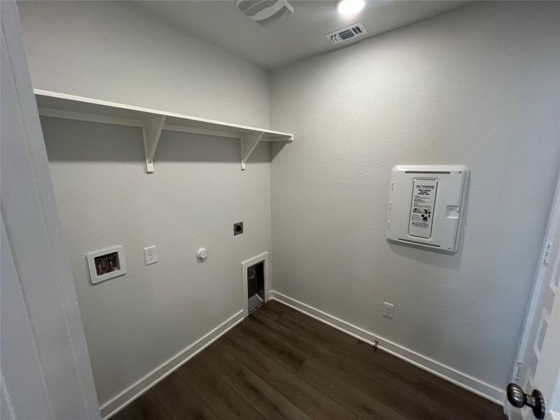 Functional laundry room featuring sturdy shelving and rich wood-tone flooring.