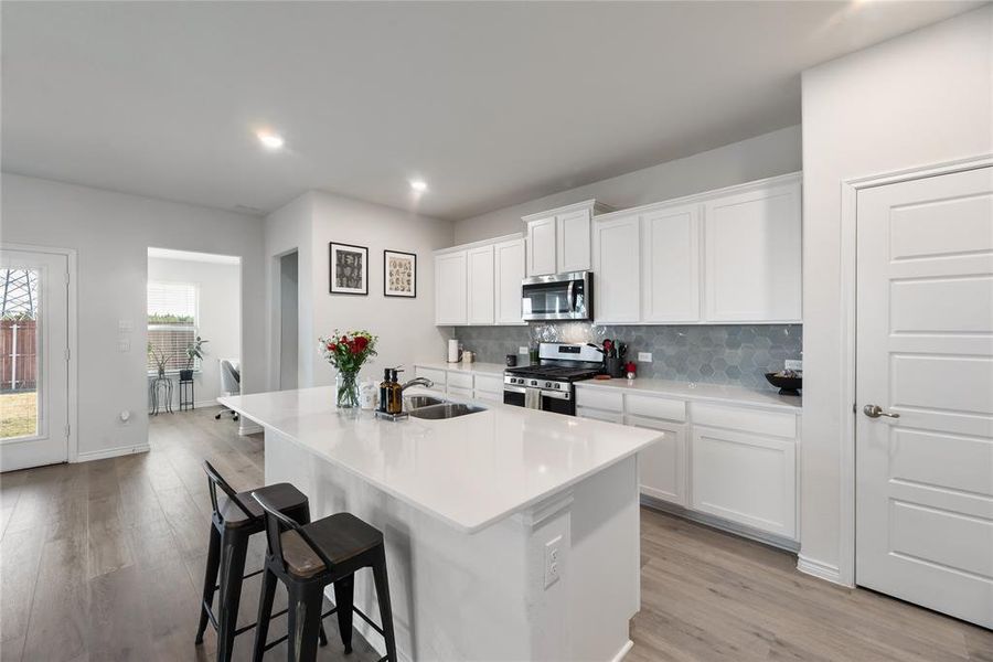 Kitchen featuring white cabinets, appliances with stainless steel finishes, a center island with sink, a kitchen breakfast bar, and recessed lighting