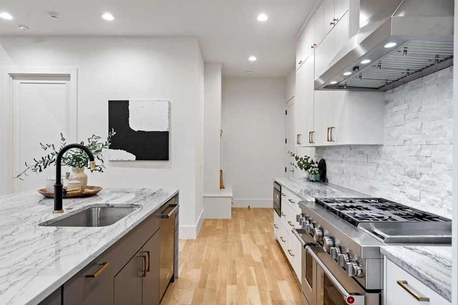 Kitchen featuring wall chimney exhaust hood, stainless steel appliances, light wood-style flooring, white cabinetry, and recessed lighting Kitchen featuring wall chimney exhaust hood, stainless steel appliances, light wood-style flooring, white cabinetry, and recessed lighting