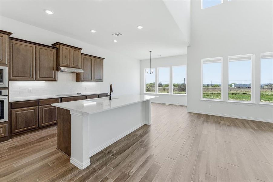 Kitchen with wood tiled floors, a kitchen island with sink, stainless steel appliances, light stone countertops, and backsplash Kitchen with wood tiled floors, a kitchen island with sink, stainless steel appliances, light stone countertops, and backsplash