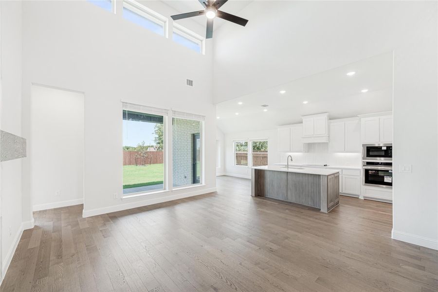 Open-concept living area with high ceilings, hardwood floors, and kitchen with white cabinets and center island