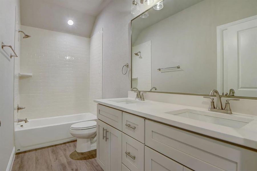 Full bath featuring shower / bathtub combination, wood finished floors, toilet, and double vanity