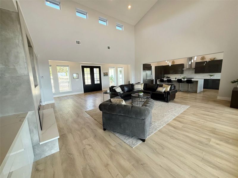 Living room with light wood-style floors, a towering ceiling, french doors, and recessed lighting