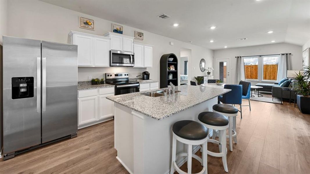 Kitchen featuring stainless steel appliances, white cabinetry, a breakfast bar area, open floor plan, and light stone countertops Kitchen featuring stainless steel appliances, white cabinetry, a breakfast bar area, open floor plan, and light stone countertops