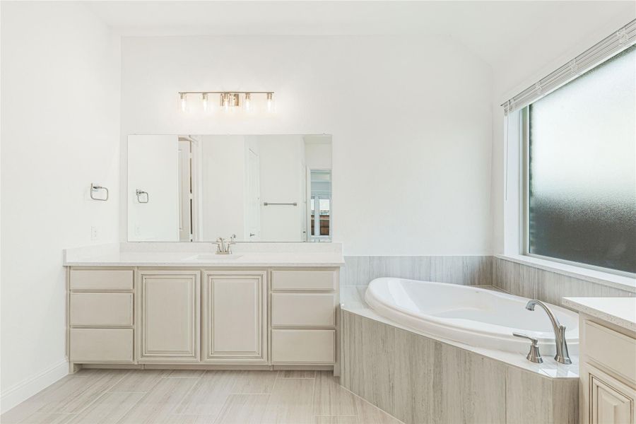 Master bathroom with corner soaking tub, single-sink vanity, large mirror, and tile surround in neutral tones
