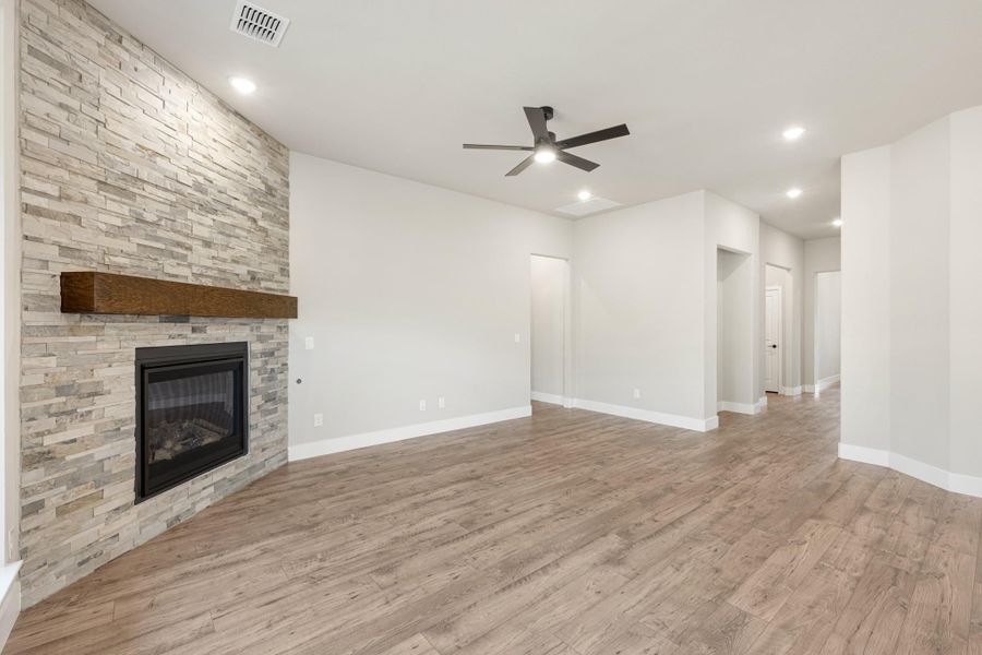 Open living room with stacked stone fireplace, wood mantel, ceiling fan, and light hardwood floors