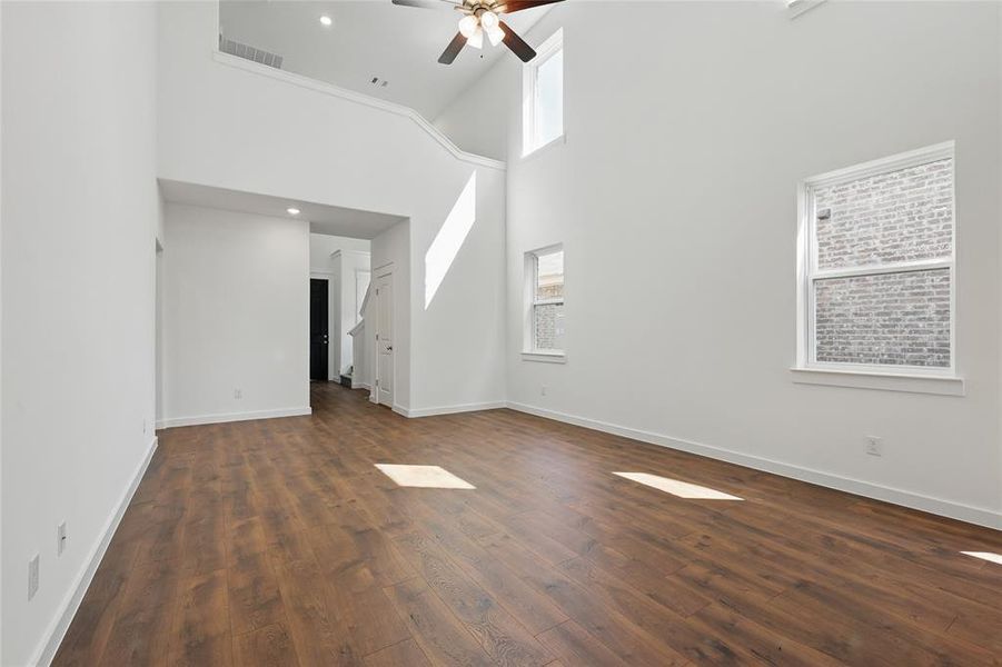 Unfurnished living room featuring healthy amount of natural light, dark wood finished floors, a towering ceiling, a ceiling fan, and recessed lighting