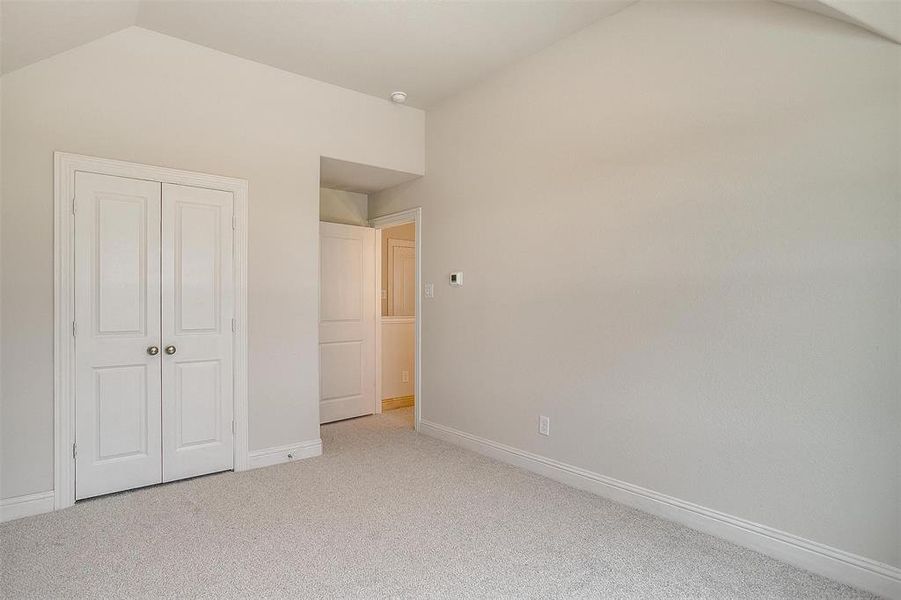 Unfurnished bedroom featuring lofted ceiling, a closet, and light carpet