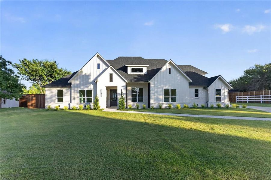 Modern farmhouse-style residence with a white brick and board-and-batten facade, dark-framed windows, a black roof, and a prominent front entry with a dark door Modern farmhouse-style residence with a white brick and board-and-batten facade, dark-framed windows, a black roof, and a prominent front entry with a dark door