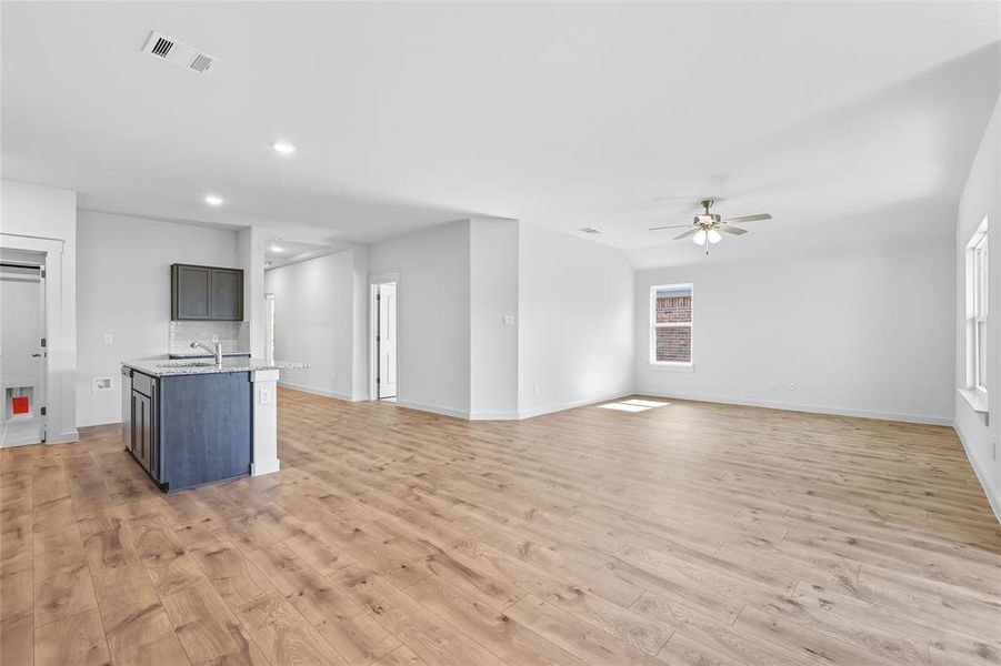 Kitchen with a center island with sink, light stone counters, open floor plan, light wood finished floors, and recessed lighting