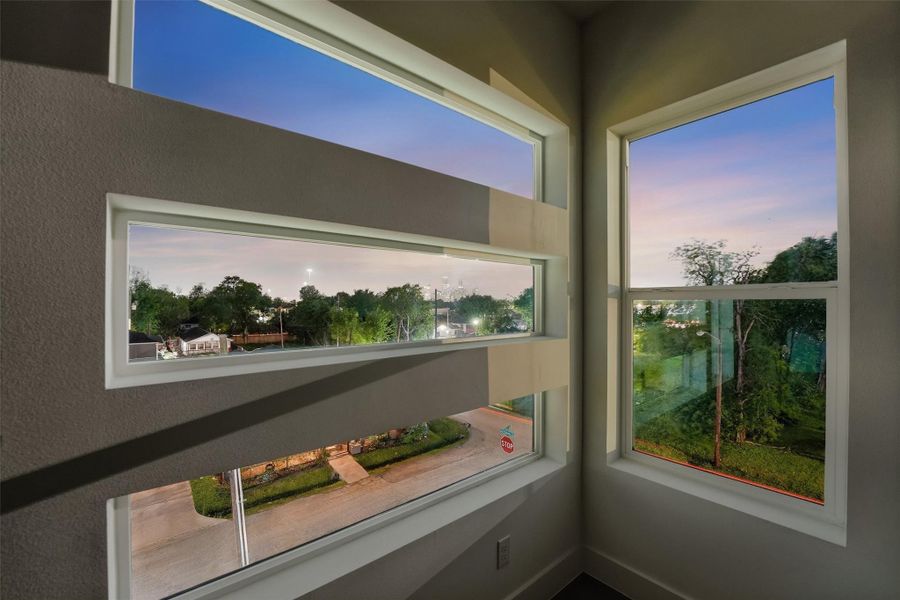 Bright architectural corner featuring stacked clerestory windows and oversized panes that frame serene neighborhood and skyline twilight views, filling the space with natural light and modern design appeal.