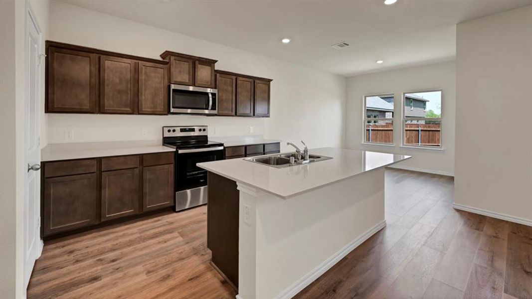 Kitchen featuring an expansive island with an undermount double-basin sink, dark wood-finish cabinetry, stainless steel appliances, and wood-finish flooring