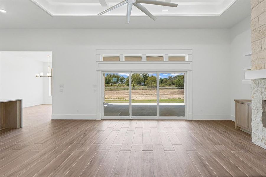Unfurnished living room featuring light wood-type flooring, a ceiling fan, a chandelier, and a stone fireplace Unfurnished living room featuring light wood-type flooring, a ceiling fan, a chandelier, and a stone fireplace