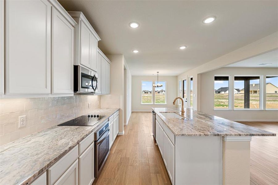 Kitchen with light stone countertops, white cabinets, stainless steel appliances, light wood-type flooring, and decorative backsplash