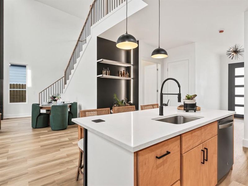 Kitchen with a kitchen breakfast bar, hanging light fixtures, a center island with sink, light wood-style floors, and light stone counters