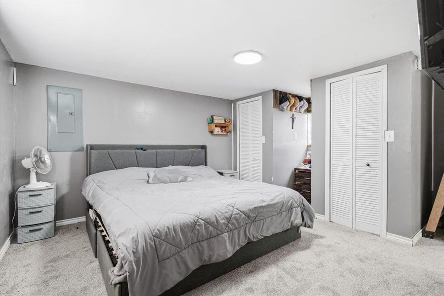 Bedroom with multiple closets, electric panel, and carpet flooring