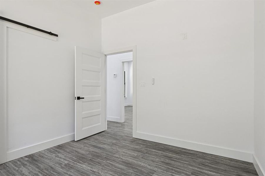 Unfurnished bedroom featuring a barn door and dark wood-style flooring Unfurnished bedroom featuring a barn door and dark wood-style flooring