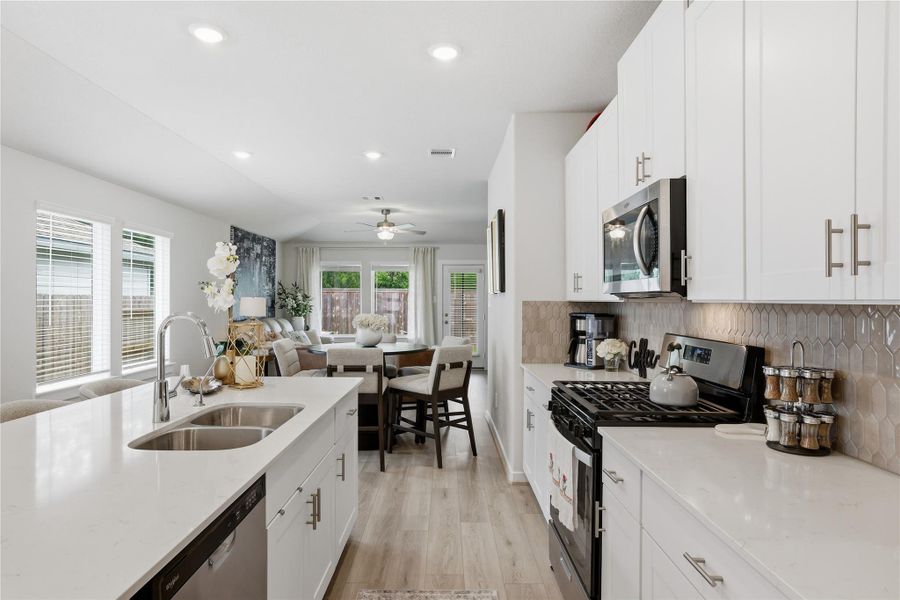 This bright, open-concept kitchen and living area features modern white cabinetry, stainless steel appliances, and sleek countertops. The space flows seamlessly into a cozy living room with large windows, offering ample natural light and views of the fenced backyard.