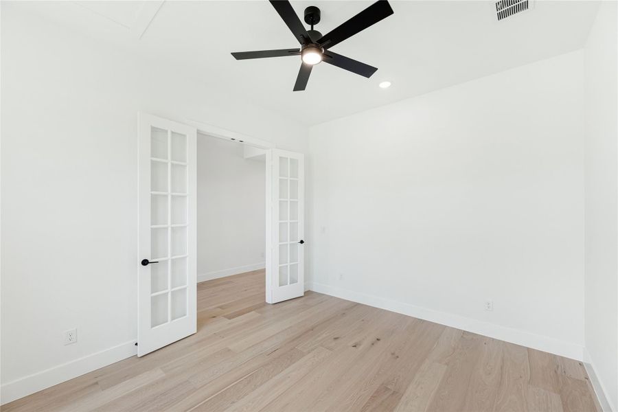 Empty room with light wood floors, black ceiling fan, and white French doors leading to a closet