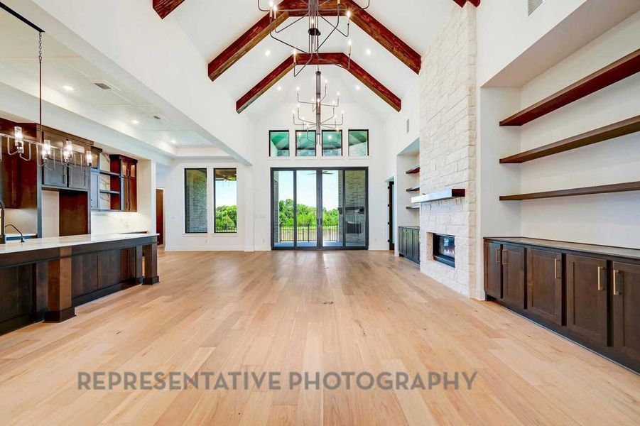 Unfurnished living room featuring a chandelier, light wood-style floors, a fireplace, high vaulted ceiling, and beamed ceiling Unfurnished living room featuring a chandelier, light wood-style floors, a fireplace, high vaulted ceiling, and beamed ceiling