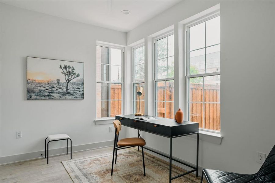Light-filled room featuring multiple large windows, wood-finish flooring, and white wall finishes Light-filled room featuring multiple large windows, wood-finish flooring, and white wall finishes