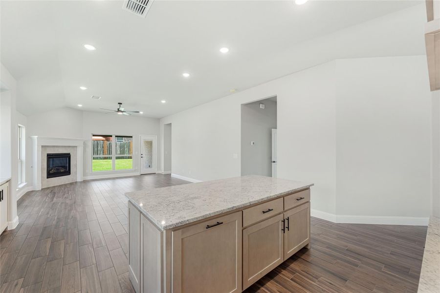 Open-concept kitchen and living area with granite island, wood-look floors, and fireplace with vaulted ceiling Open-concept kitchen and living area with granite island, wood-look floors, and fireplace with vaulted ceiling