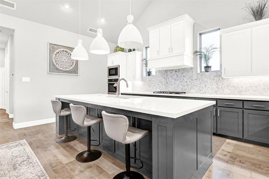 Kitchen with backsplash, decorative light fixtures, a breakfast bar area, light wood-type flooring, and lofted ceiling Kitchen with backsplash, decorative light fixtures, a breakfast bar area, light wood-type flooring, and lofted ceiling