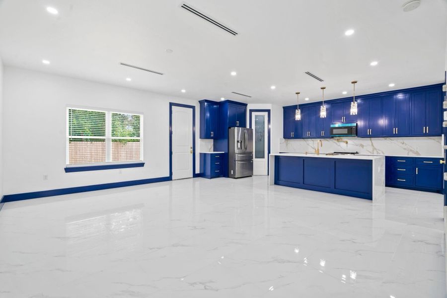 Another angle of the expansive open-concept living space showcases striking blue kitchen cabinetry, sleek quartz countertops, and elegant porcelain flooring. Recessed lighting paired with stylish pendant fixtures fills the home with a bright, airy feel. The thoughtfully designed layout flows seamlessly, while refined architectural details add character and visual appeal throughout.