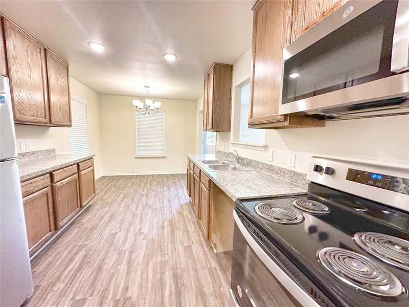 Kitchen with pendant lighting, sink, a notable chandelier, light hardwood / wood-style flooring, and stainless steel appliances