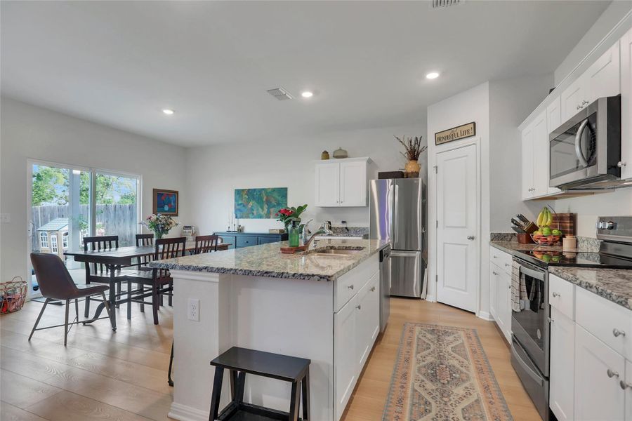 Kitchen featuring stainless steel appliances, white cabinets, light wood-style floors, light stone countertops, and large kitchen island.