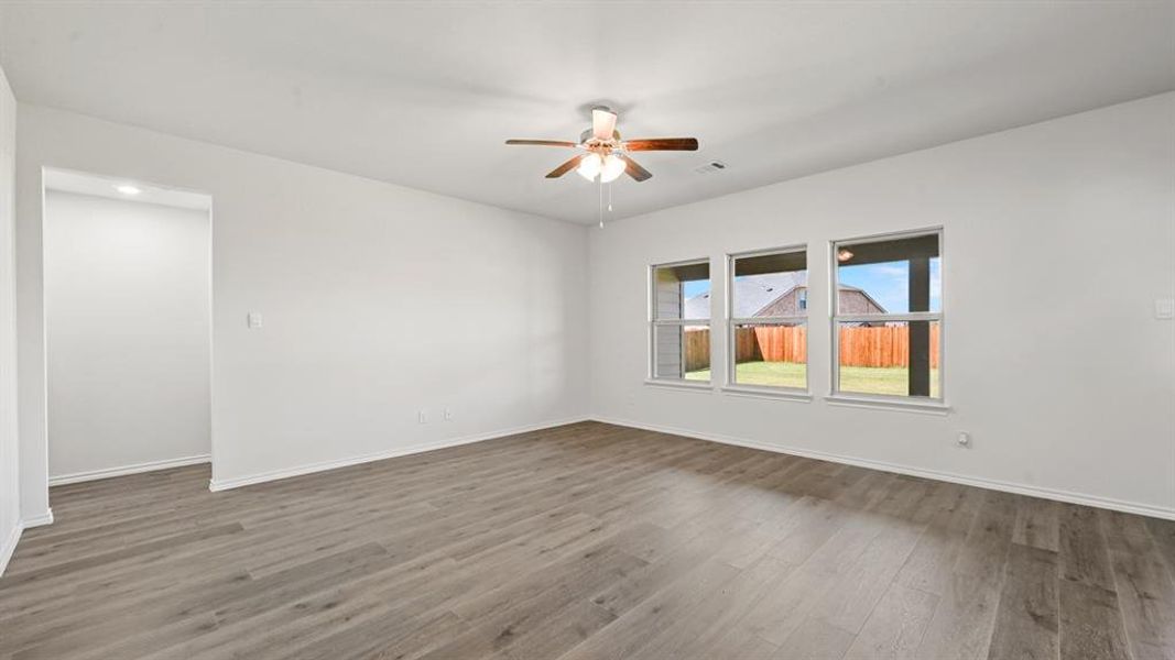 Spacious room featuring wood-finish flooring, white walls, and a ceiling fan