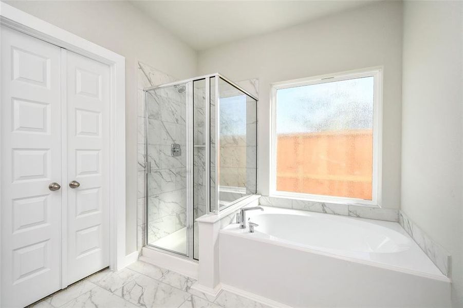 Escape to a spa-like oasis in this primary bathroom. Enjoy a walk-in shower with tile surround, a separate garden tub with custom detailing, and an elegant vanity featuring light countertops, modern hardware, and bright recessed lights. Experience luxury and relaxation in every detail. Sample photo of completed home with similar floor plan. Actual colors and selections may vary.