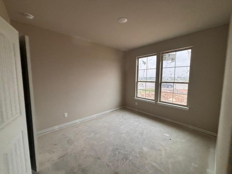 Interior room featuring neutral paint, two windows with grids, white trim, and a concrete subfloor