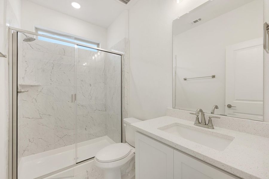 Bathroom with marble-tiled shower, glass doors, white vanity with quartz countertop, and toilet