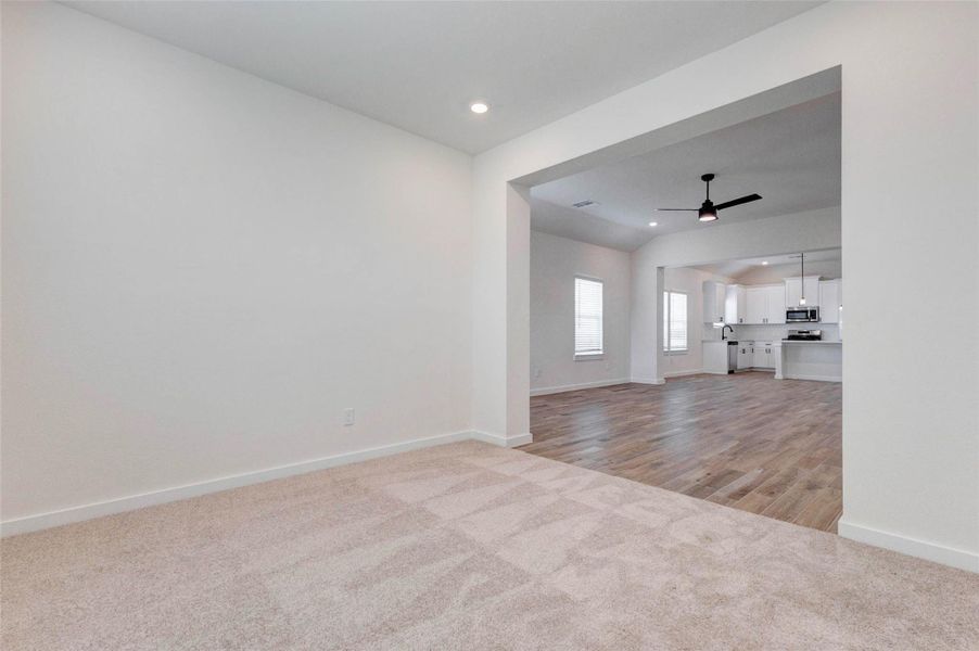 This inviting living space offers a clear view back toward the entry and adjacent rooms, showcasing the home’s thoughtful, open layout. A modern ceiling fan adds comfort and style, while the combination of tile flooring and soft carpeted transitions defines each space. Natural light and clean finishes create a bright, welcoming atmosphere throughout.