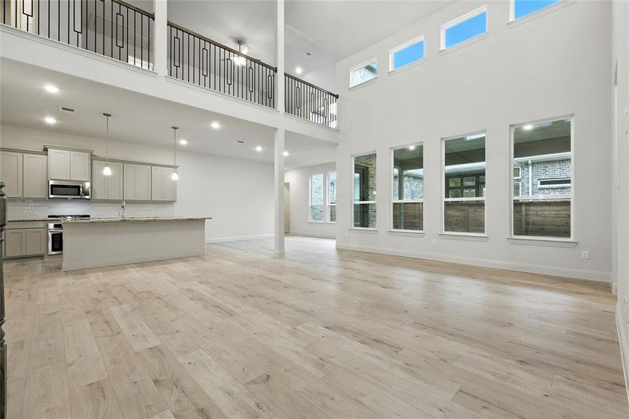 Unfurnished living room featuring light wood-type flooring, a towering ceiling, and recessed lighting