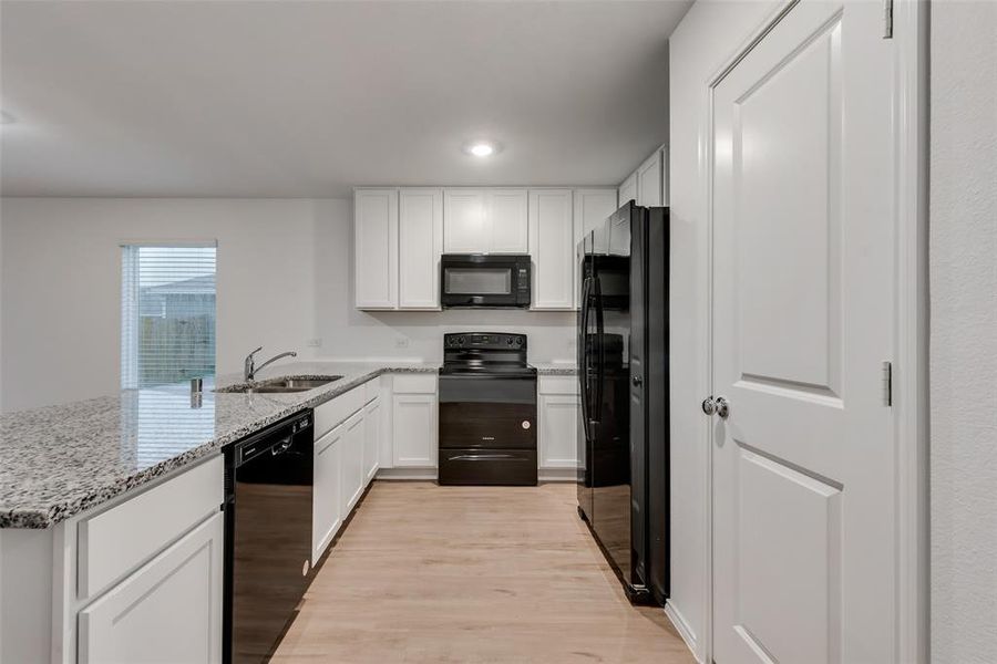 Kitchen with sink, light wood-type flooring, light stone counters, kitchen peninsula, and black appliances