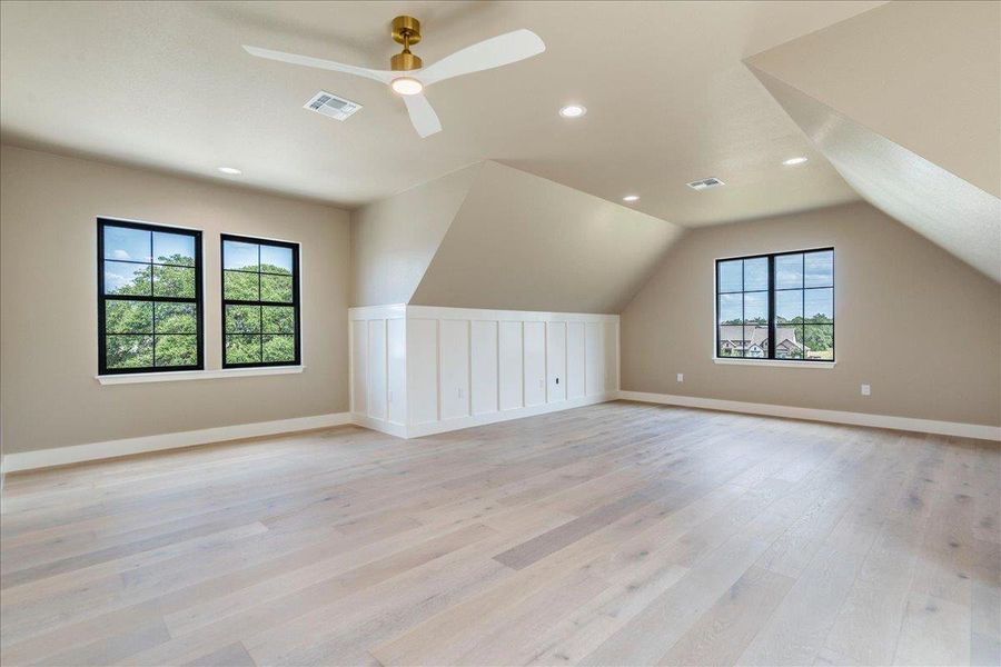 A spacious room offers light wood flooring, white paneling, and multiple windows.