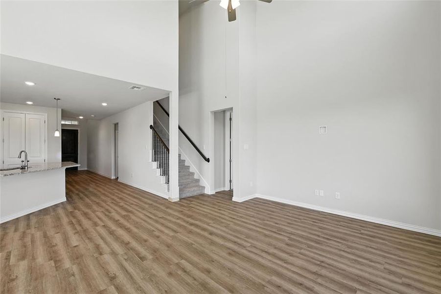 Unfurnished living room featuring stairway, wood finished floors, recessed lighting, ceiling fan, and a high ceiling Unfurnished living room featuring stairway, wood finished floors, recessed lighting, ceiling fan, and a high ceiling