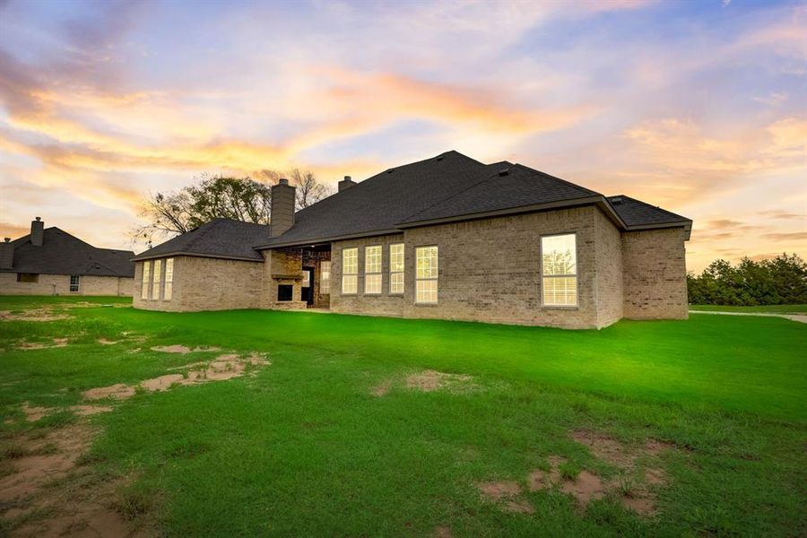 Back of house with a lawn, a chimney, a shingled roof, and brick siding Back of house with a lawn, a chimney, a shingled roof, and brick siding