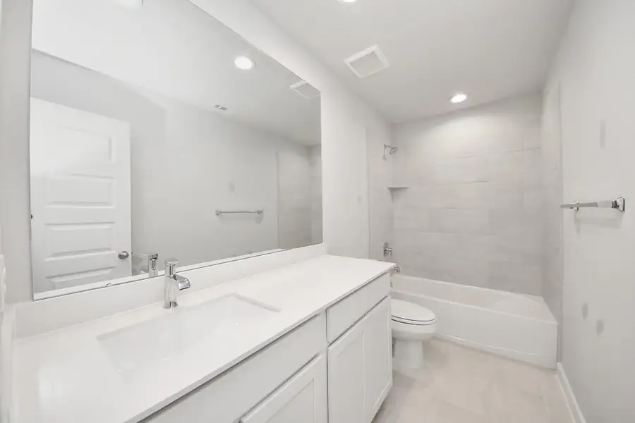 Secondary bath features tile flooring, bath/shower combo with tile surround, light stained wood cabinets, beautiful light countertop. Sample photo of completed home with similar floor plan. Actual colors and selections may vary.