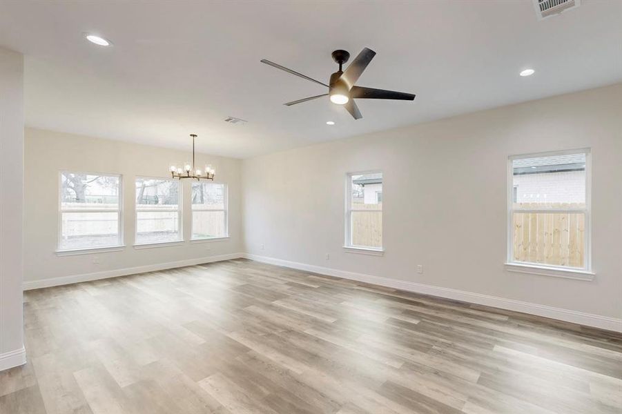 Empty room with ceiling fan with notable chandelier and light hardwood / wood-style floors